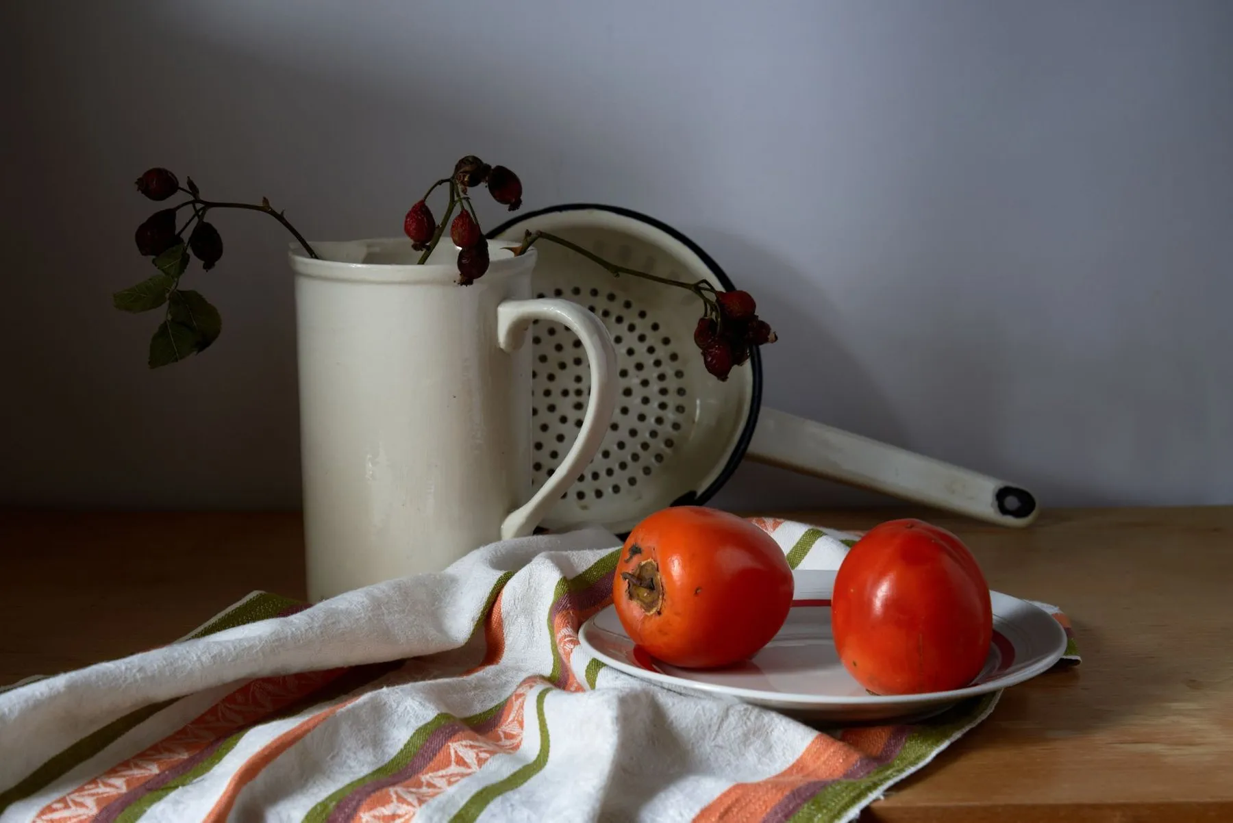 Enamel jug and colander with tomatoes on a folded tea towel