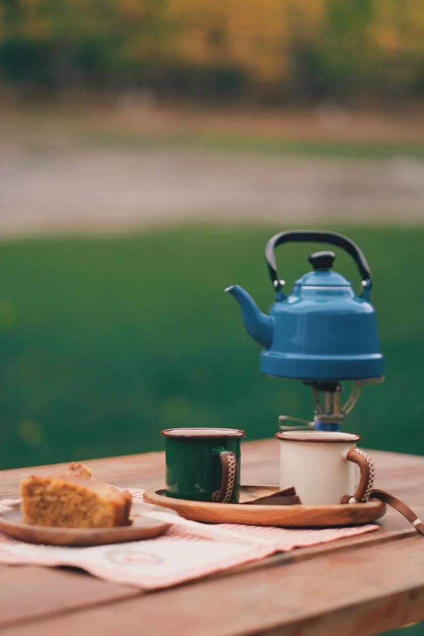 A blue enamel kettle on a camp stove beside two enamel mugs on an outdoor table