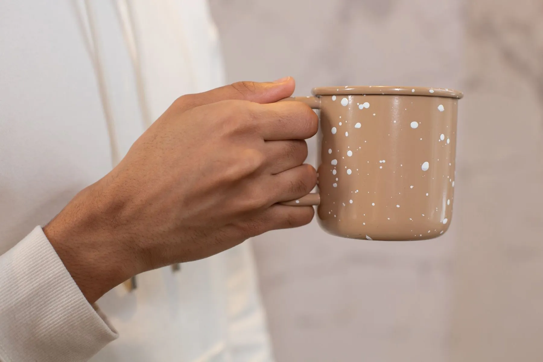 A hand holding a speckled enamel mug by its handle